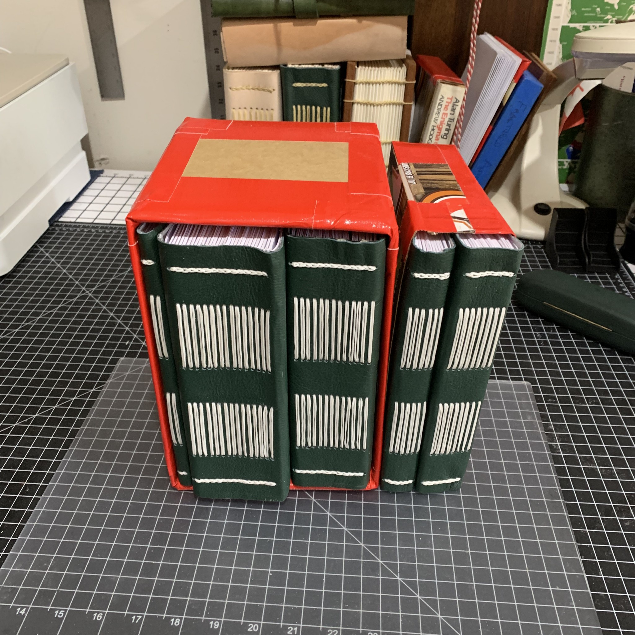 A printed edition of ‘Form & Number: A History of Mathematical Beauty’, bound into five volumes with green leather covers and visible white stitching. The volumes are placed into temporary slipcases. The left-hand first volume (front matter) is slim; the second and third volumes (parts I+II) are 5–6cm thick; the fourth and fifth volumes (part III and part IV+bibliography+index) are 2–3cm thick.